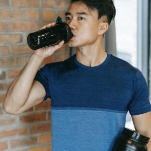 Determined young ethnic guy drinking water during training in gym