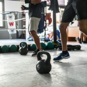 Man in Black T-shirt and White Shorts Holding Black Kettle Bell